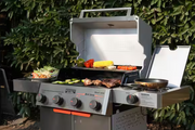 Asador de gas Monument Grills de 4 quemadores, tapa abierta y parrilla con comida